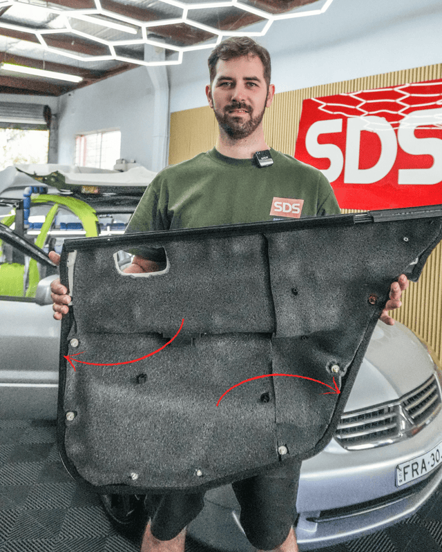 Person holding a car door panel with red arrows in a garage setting, featuring an SDS logo.